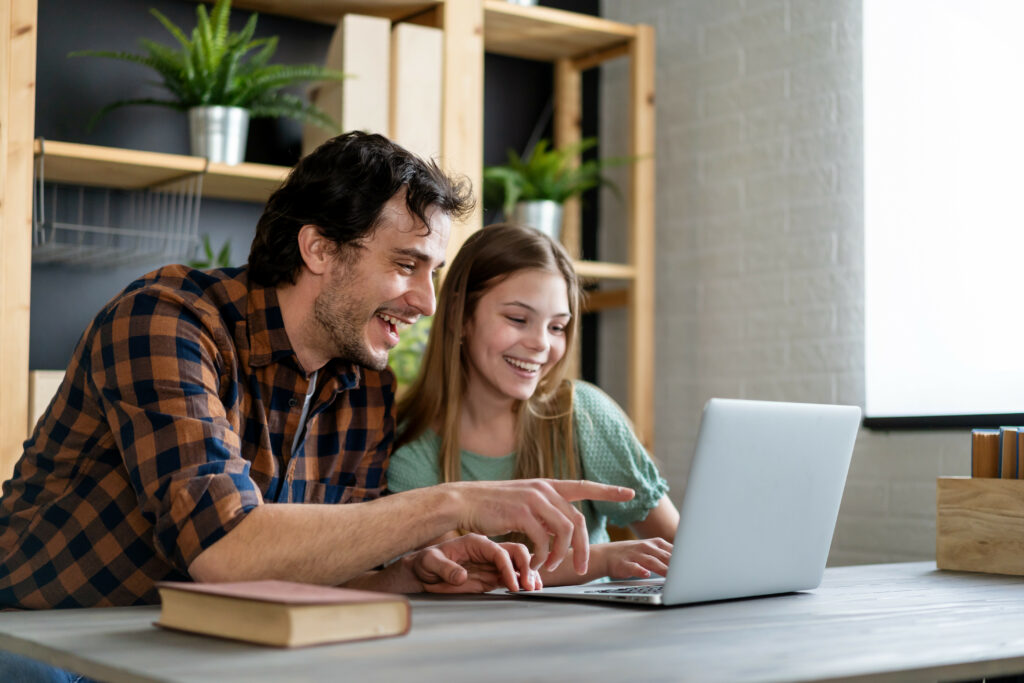 Vater und Tochter sitzen lachend vor einem Laptop